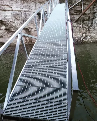 Metal bridge over water near rocky cliff.