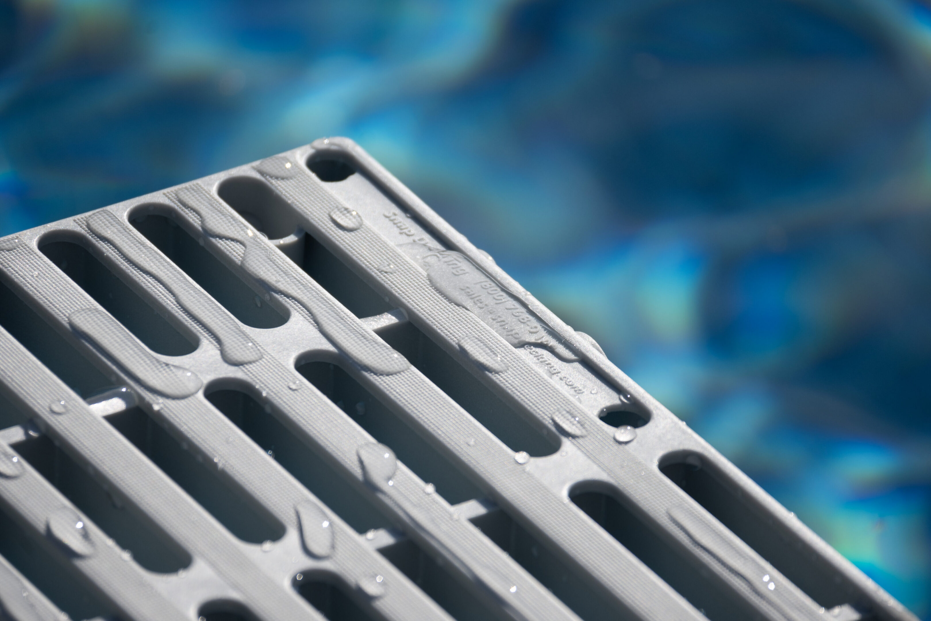 Wet poolside grate with blurred water background.