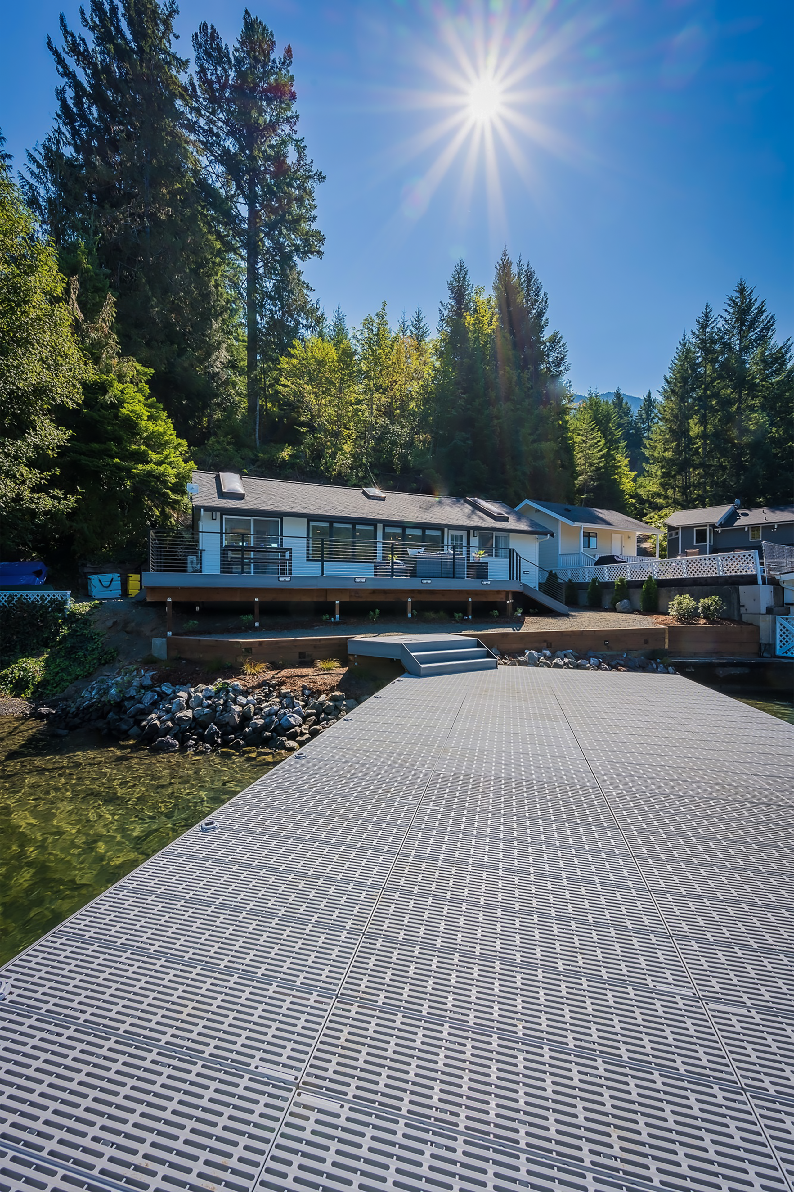 Lakeside house with sunlit dock and trees.